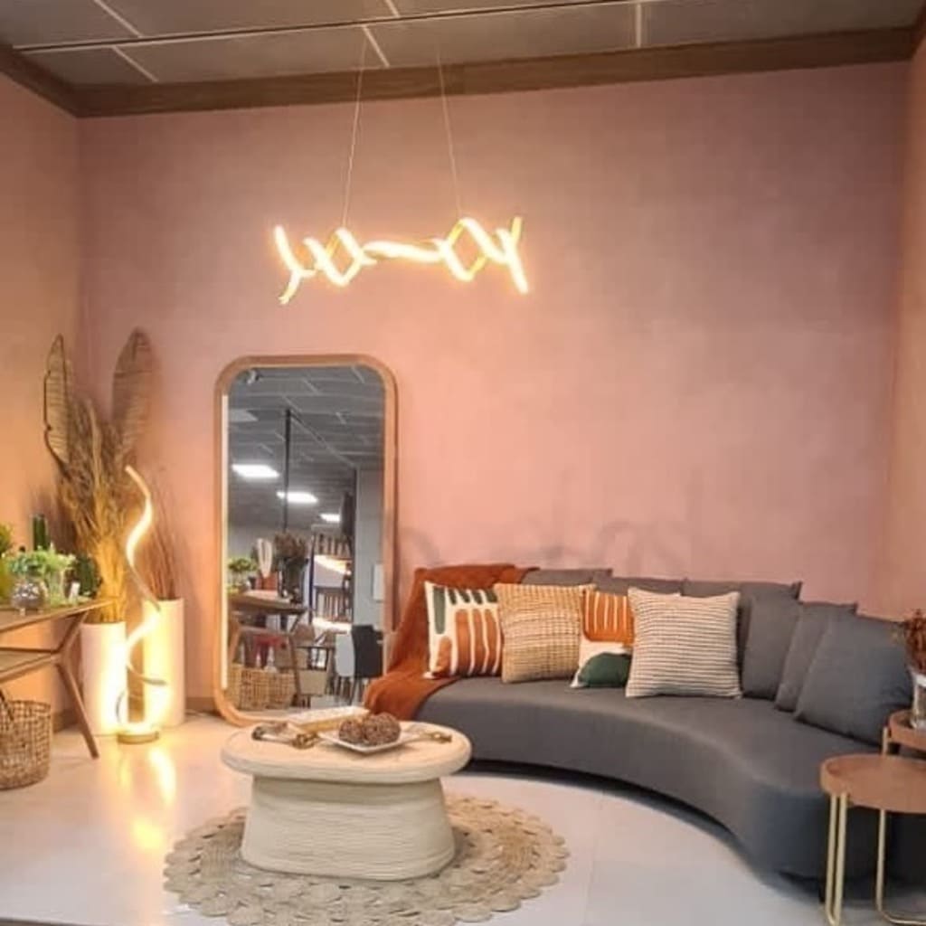 sala com parede rosé gold, sofá com almofadas coloridas, espelho, LED e mesa de centro