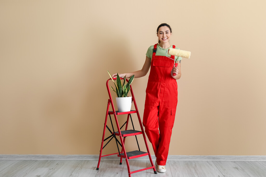 mulher com escada e rolo de tinta para reformar casa com um dos tipos de tinta para parede